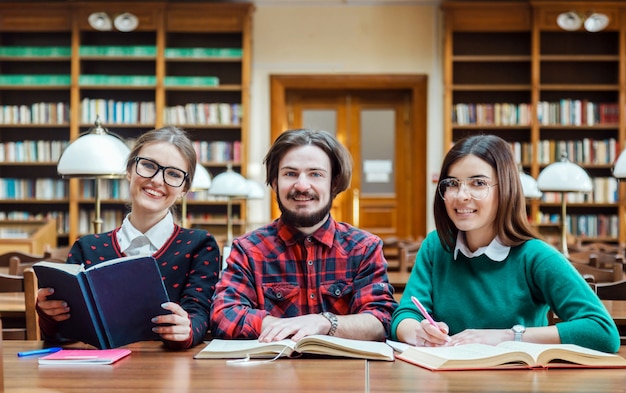 Счастливые студенты в библиотеке, улыбаясь в камеру