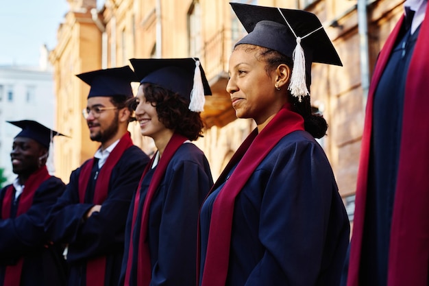 Photo happy students in robes standing in a row and listening to speaker