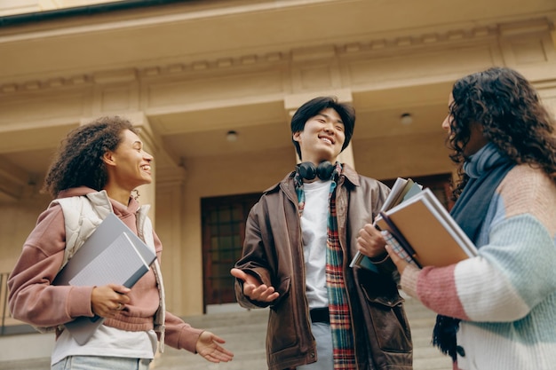 Photo happy students talking each other standing near university campus and holding books and laptop