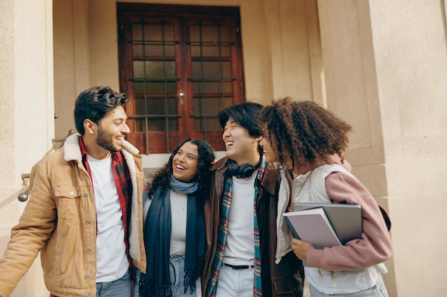 Photo happy students talking each other standing near university campus and holding books and laptop