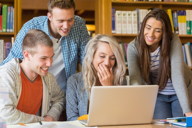 Happy students using laptop at desk in library