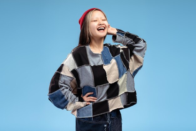 Photo happy stylish asian teenager girl in red hat posing with closed eyes isolated on blue