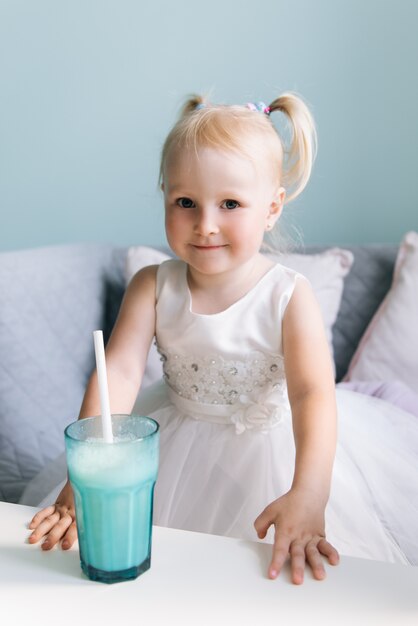 Happy stylish baby girl in a children's cafe drinking a milkshake