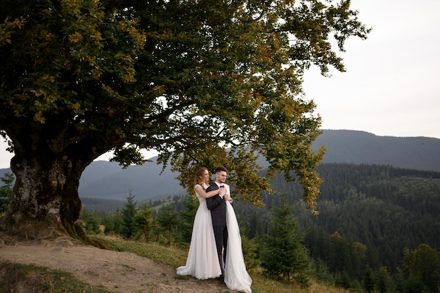 Happy stylish bride and groom running and having fun in mountains on summer sunny day