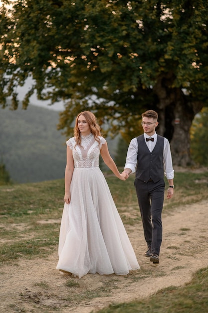 Happy stylish bride and groom running and having fun in mountains on summer sunny day