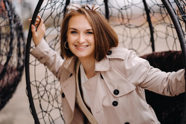 A happy stylish girl In a gray coat is sitting outside in an armchair