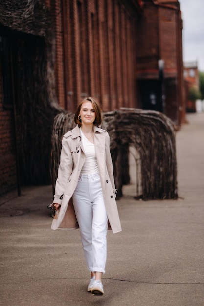 A happy stylish girl in a gray coat walks around the city