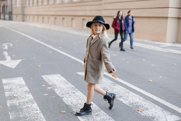 Happy stylish girl in a hat walks and poses as a model on the waterfront near the pedestrian