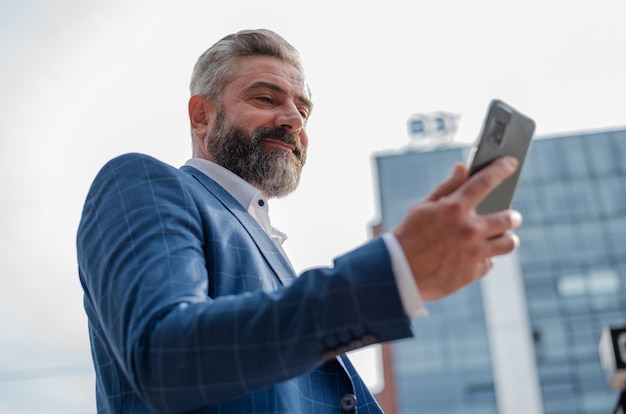 A happy stylish mature business man using a phone in the city with urban buildings in the background