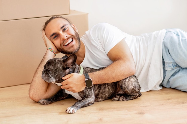 Happy stylish millennial guy caressing his dog in new apartment