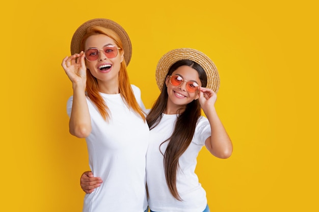 Happy stylish mother and daughter posing at studio yellow background wearing straw hat sunglasses