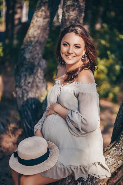 Donna incinta sorridente alla moda felice che posa nella foresta