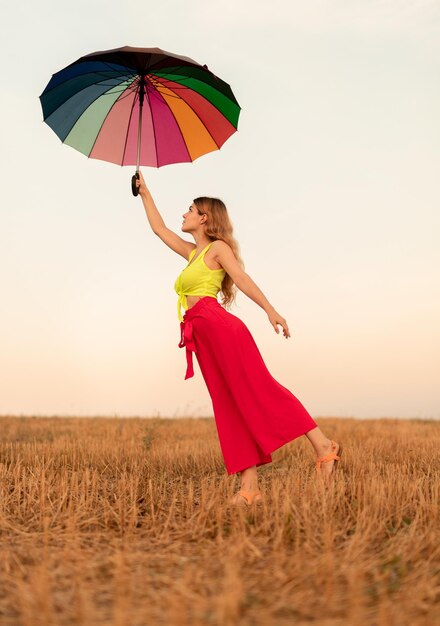 Happy stylish woman dancing with umbrella in field