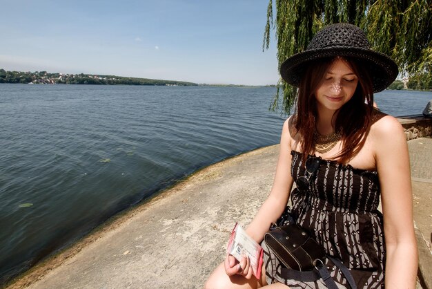 写真 テキストのための水の夏の旅行の概念スペースの近くの日当たりの良い海岸に座って幸せなスタイリッシュな女性