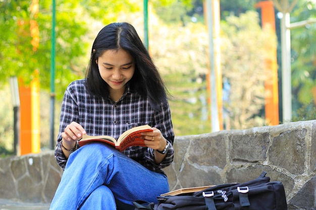 幸せで成功したアジアの女子大生が公園で本を読んで楽しんでいます