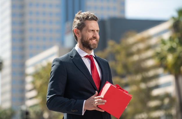 Happy successful businessman in suit hold present box standing outdoor, purchase.