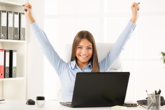 Felice imprenditrice di successo in ufficio con le braccia alzate.