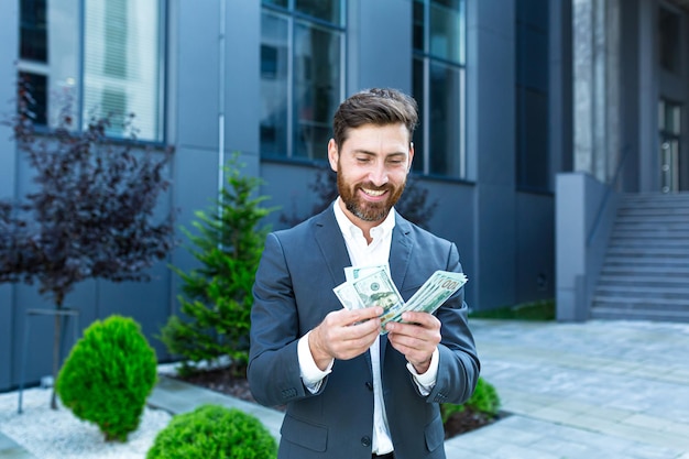 Happy successful Caucasian bearded businessman counts, waves, throws, show off, flaunt cash money background a modern office building looking at camera Celebrate Winner success in betting stock market