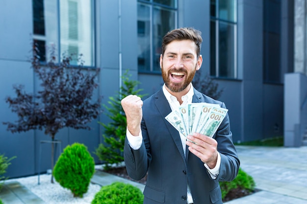 Photo happy successful caucasian bearded businessman counts, waves, throws, show off, flaunt cash money background a modern office building looking at camera celebrate winner success in betting stock market