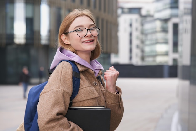 本の眼鏡で笑っている幸せな成功した大学生の生徒の若い女性は結果リストを見てください