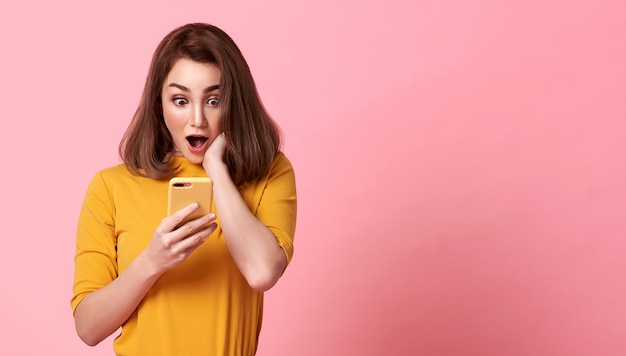 Foto giovane donna felice e sorpresa bella facendo uso del telefono cellulare sullo spazio rosa dello spazio della copia.
