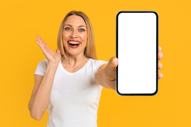 Happy surprised excited pretty millennial european blond woman in white tshirt show smartphone with