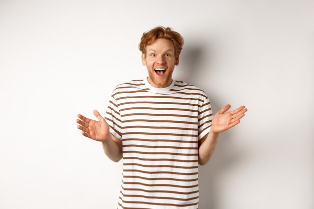 Happy and surprised redhead man rejoicing of good news, looking amazed and pleased at camera, white background.