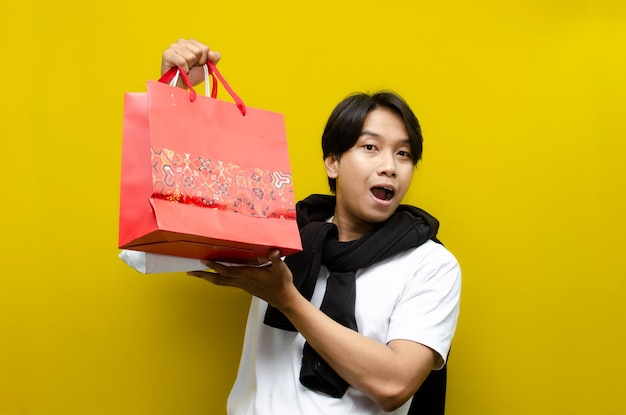 happy surprised young asian man holding shopping bags in excitement