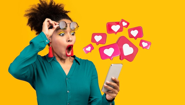 Happy surprised young black lady with open mouth has romantic chat with hearts on phone enjoys message