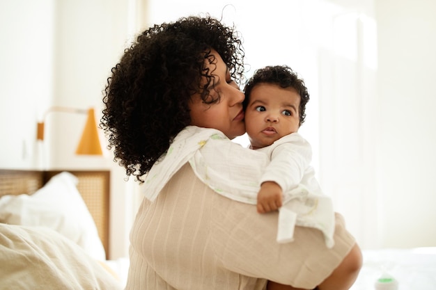 Photo happy sweet black curly millennial mother with towel kissing little baby enjoy motherhood