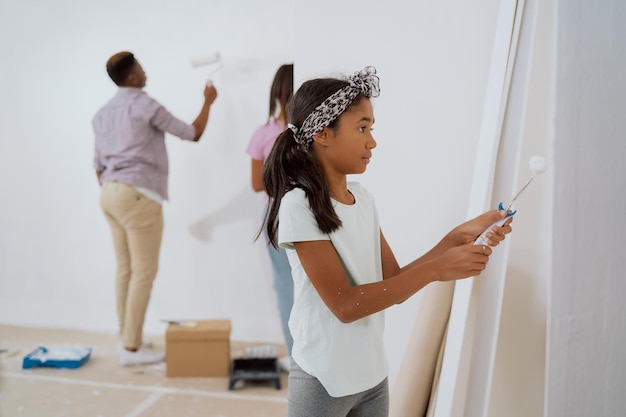 Happy sweet girl in her hands holding a roller with white paint carefully trying to paint walls