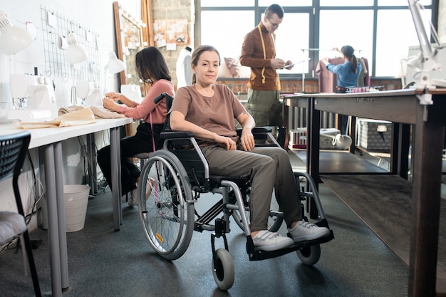 Happy tailor in wheelchair looking at you against colleagues working