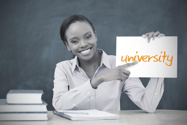 Happy teacher holding page showing university in her classroom at school