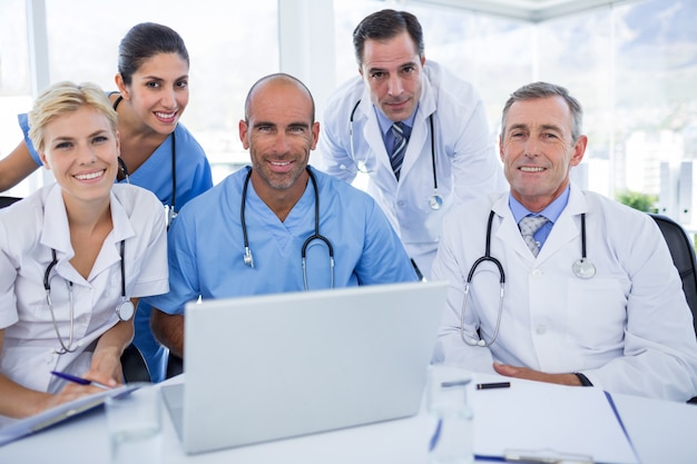 Happy team of doctors looking at camera in behind laptop computer 