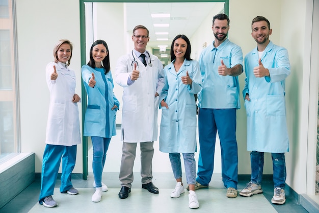 Felice team di medici moderni di successo e fiduciosi sono in posa e guardando la telecamera nel corridoio dell'ospedale