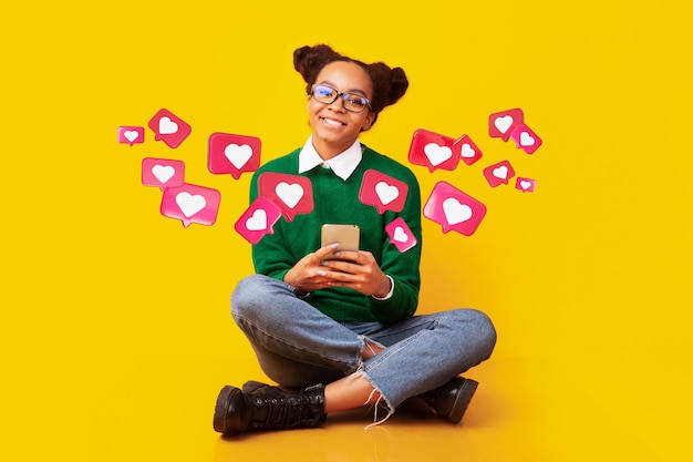 Photo happy teen african american female in glasses has romantic chat with hearts on phone enjoys message