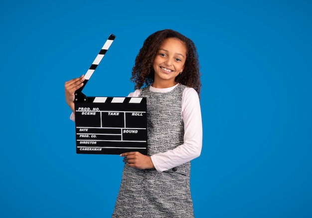 ビデオの撮影を開始するカチンコを叩いて幸せな 10 代のアフリカ系アメリカ人の女の子