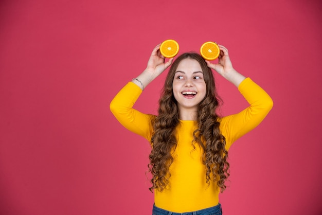 Happy teen child hold orange fruit on pink background