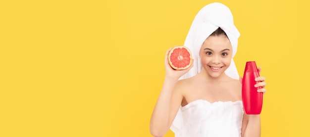 Happy teen child in towel with grapefruit shampoo bottle on yellow background Cosmetics and skin care for teenager child poster design Beauty kid girl banner with copy space