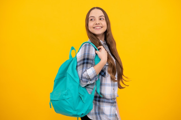 Happy teen girl in checkered shirt with backpack on yellow background, school