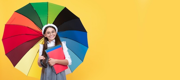 Happy teen girl under colorful umbrella in autumn season hold notebook back to school Child with autumn umbrella rainy weather horizontal poster banner with copy space