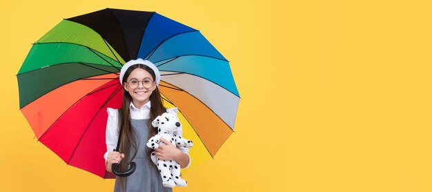 Happy teen girl under colorful umbrella in autumn season hold toy Child with autumn umbrella rainy weather horizontal poster banner with copy space