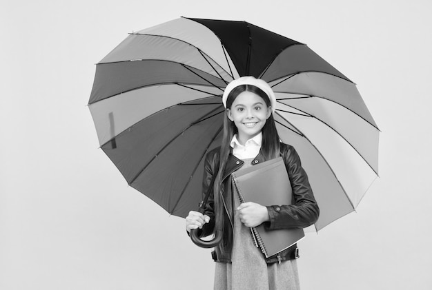 Happy teen girl under colorful umbrella for rain protection in autumn season hold notebook study