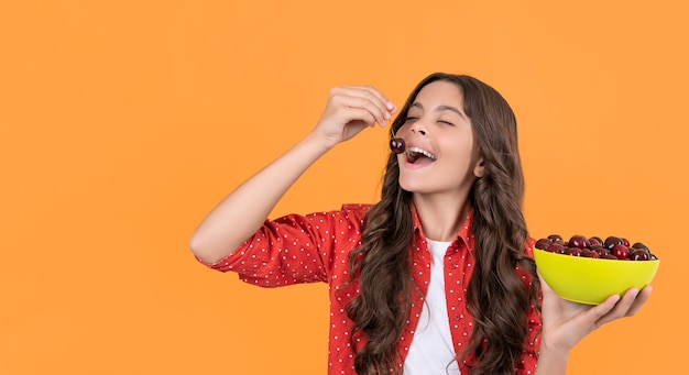 Happy teen girl eat cherry bowl on yellow background copy space