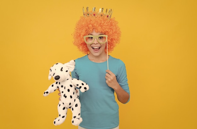 Happy teen girl in fancy clown wig wear queen crown and funny party glasses hold toy childhood