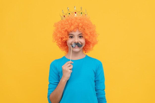 멋진 광대 가발을 쓴 행복한 십대 소녀는 4월 1일 여왕의 왕관과 재미있는 파티 콧수염을 착용합니다.