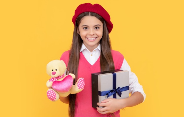 Happy teen girl in french beret hold toy present and gift box on yellow background black friday