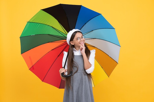 Happy teen girl in glasses and beret under colorful umbrella for rain protection in autumn season, rainy weather.