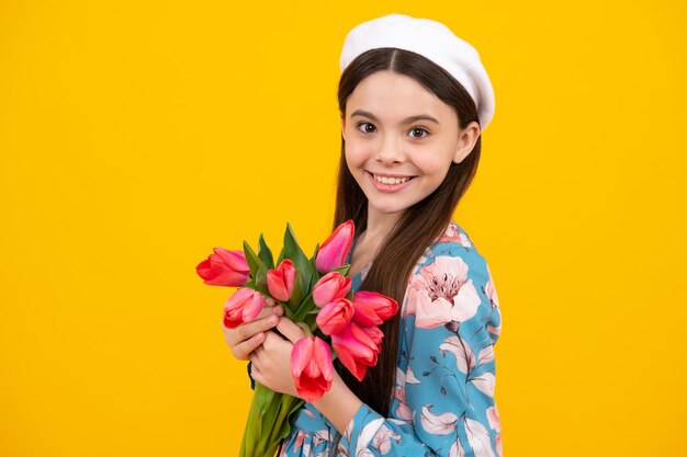 Happy teen girl in hat hold spring tulip flowers on yellow background