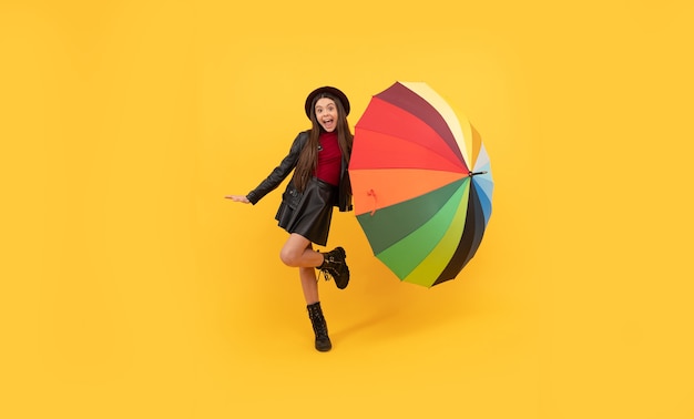 Happy teen girl in hat and leather clothes having fun with rainbow umbrella, autumn fun.